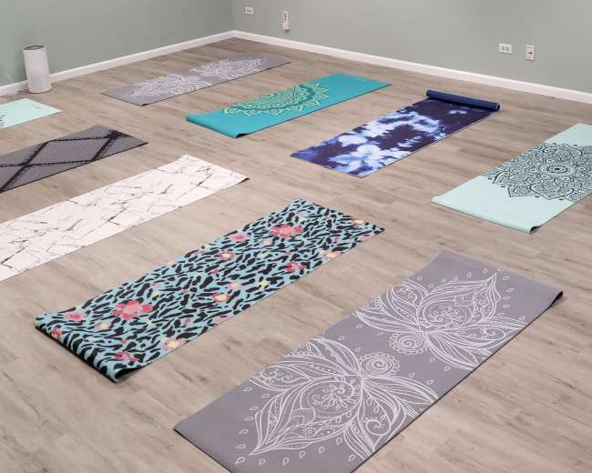 A quiet yoga studio with multiple yoga mats arranged in a grid pattern on a wooden floor, surrounded by pale green walls.