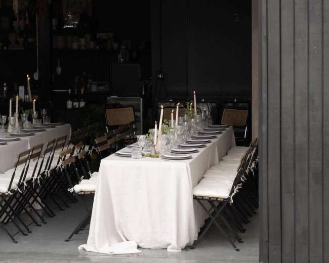 A long dining table is set up inside a dimly lit space with string lights visible overhead.