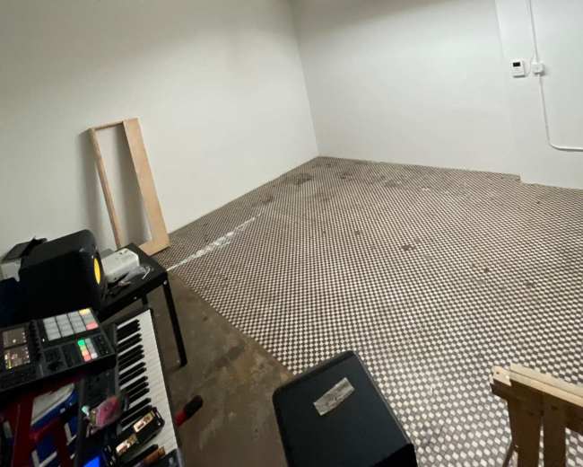 The image shows an empty room with a light-colored wall, tiled floor, and a few scattered items including a keyboard and equipment.