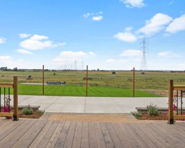 The image shows a wooden deck overlooking a grassy field with power lines and distant structures in the background.