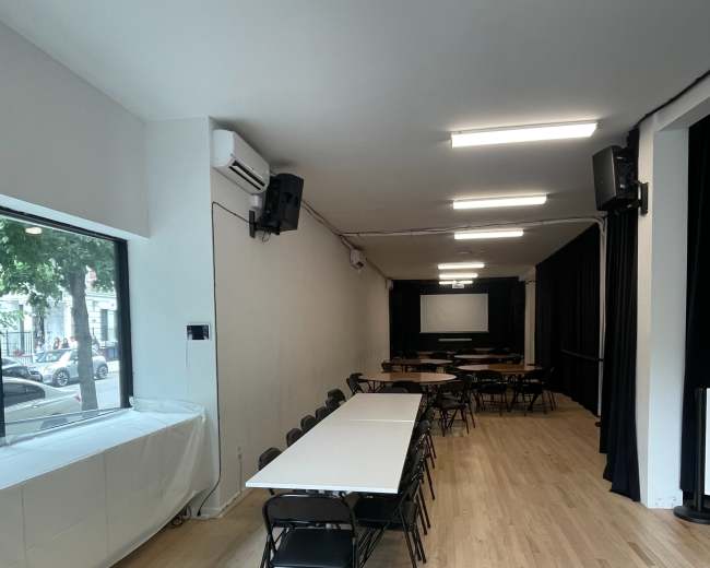The image shows a spacious, well-lit meeting room with rows of tables and chairs set up for a gathering.