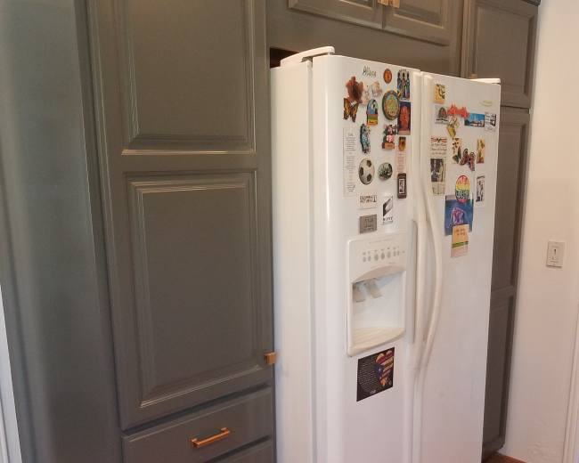 The image shows a white refrigerator located between grey cabinets and drawers in a kitchen space with tiled flooring.