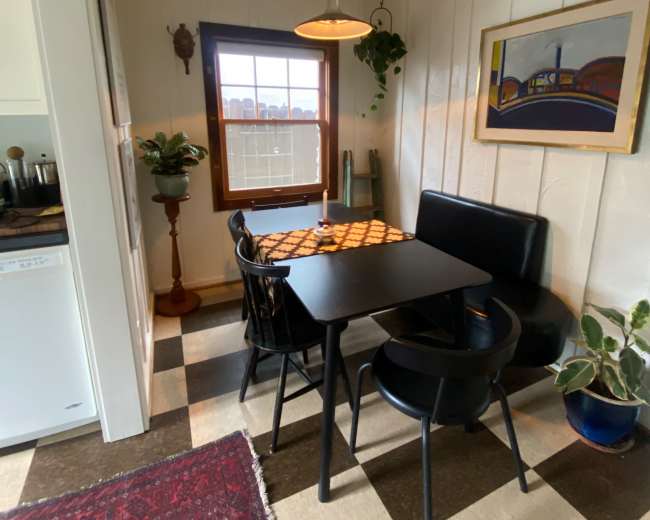 A small dining area features a black table with chairs, a window with a view, and a decorative rug on the floor.