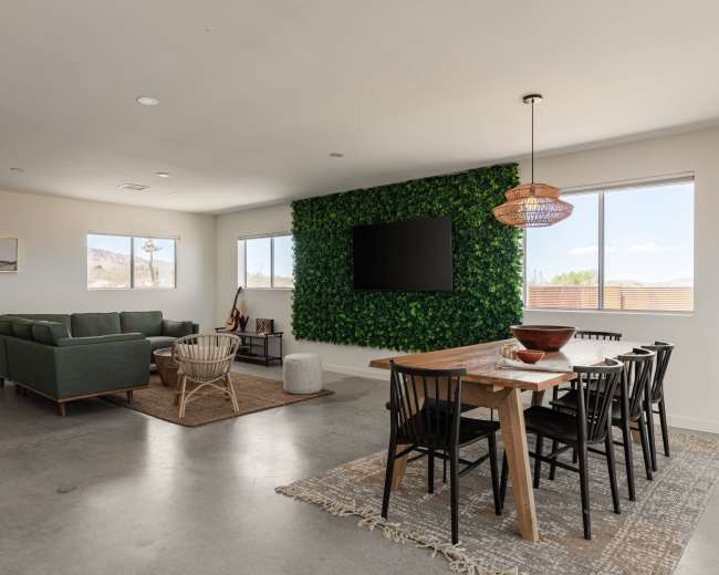 A modern living space features a green accent wall, sleek furniture, and a dining area with wooden table and black chairs.