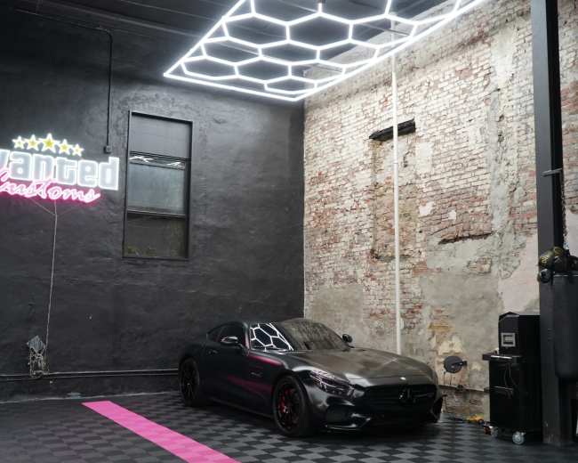 A sleek, dark-colored Mercedes-Benz is parked in a spacious room with exposed brick walls and modern geometric lighting.
