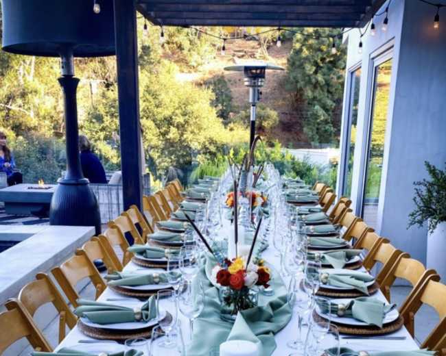 A long dining table is elegantly set with green linens, glassware, and floral centerpieces, ready for a Thanksgiving meal.