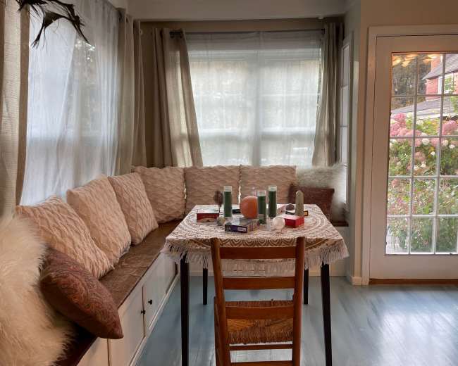 A cozy seating area features a table with various decorative items and a chair, next to large windows overlooking a garden.
