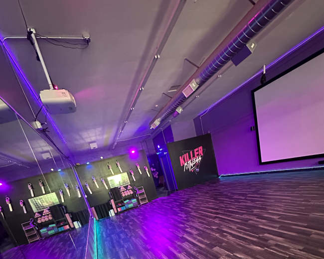 A dance studio features a mirrored wall, a projector screen, and purple ambient lighting.