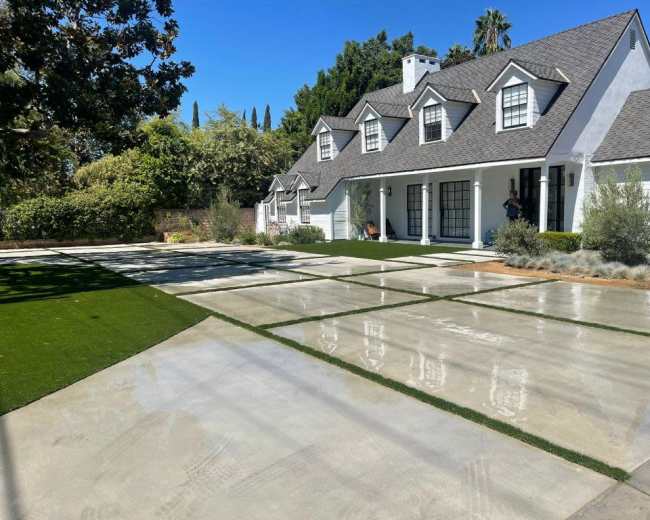 A modern house with a gray roof and white facade is surrounded by manicured lawns and a paved driveway.