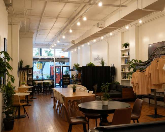 The image shows the interior of a boutique with a mix of seating areas, clothing displays on racks, and large windows revealing an outdoor view.