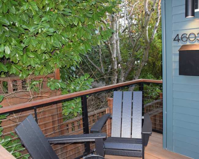 A small outdoor seating area features two black adirondack chairs and a house number sign mounted on the wall beside a mailbox.