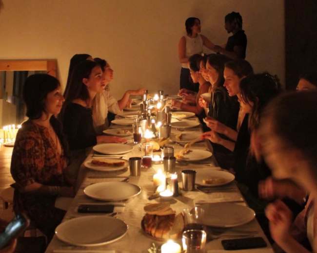 A long dining table is set with plates and candles, with a group of people engaged in conversation during a dinner gathering.