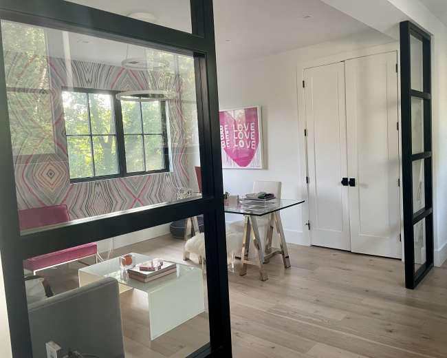 The image shows a modern office space with a glass table, a pink chair, and walls decorated with geometric patterns and motivational art.