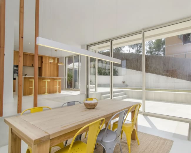 A bright dining area features a wooden table surrounded by colorful metal chairs and large glass doors leading to an outdoor space.
