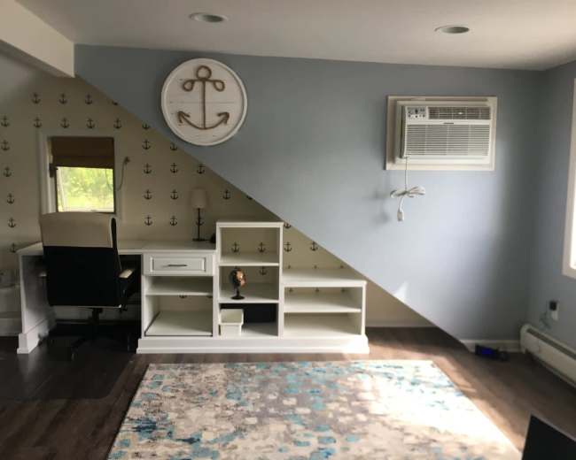 The image shows a room with a desk and shelving unit positioned against a wall featuring a nautical anchor design and an air conditioning unit mounted near the window.