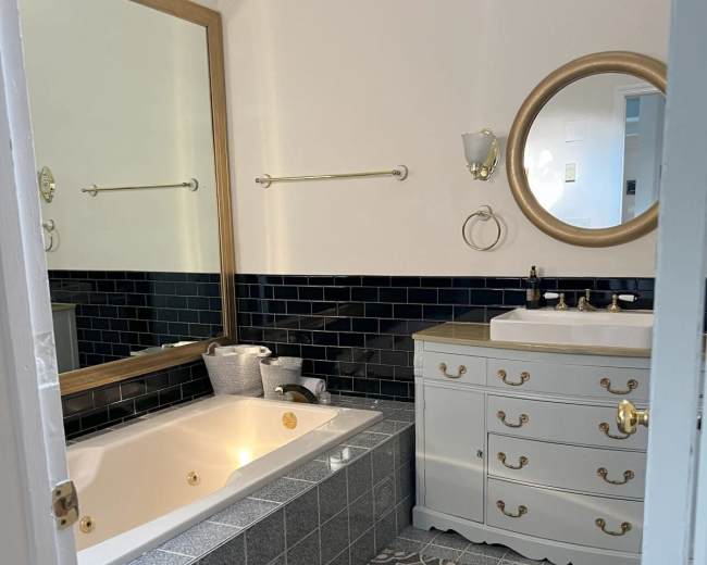The bathroom features a corner soaking tub, a large mirror, elegant fixtures, and a patterned tile floor.
