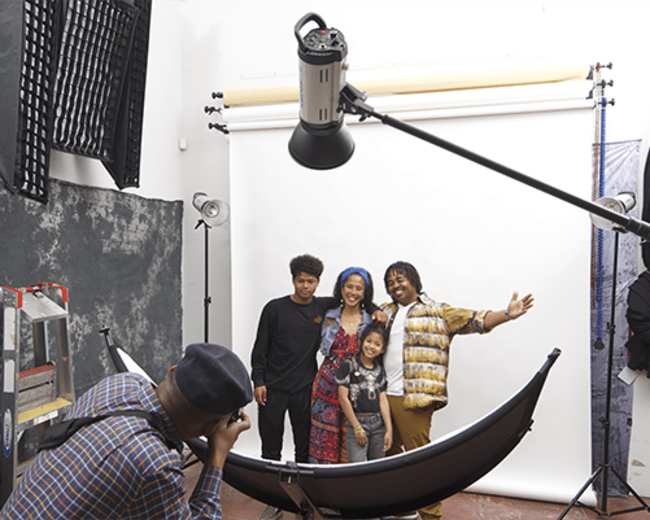 A photographer captures a group of four people posing in a studio with a large softbox and a backdrop.