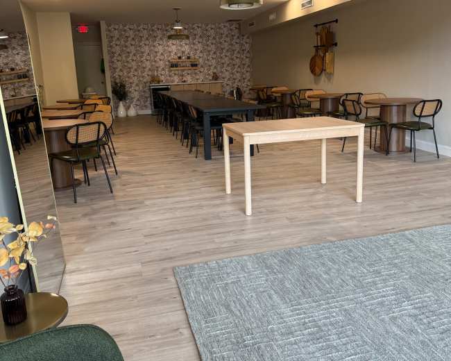 The image shows a modern café interior with a long communal table, individual seating areas, and patterned wallpaper.