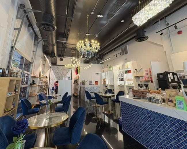 The image shows a modern cafe interior with elegant lighting, blue velvet chairs, and marble-top tables.