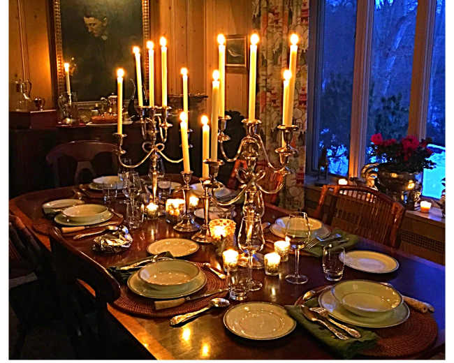 A elegantly set dining table is illuminated by candles and surrounded by warm wooden decor in a softly lit room.