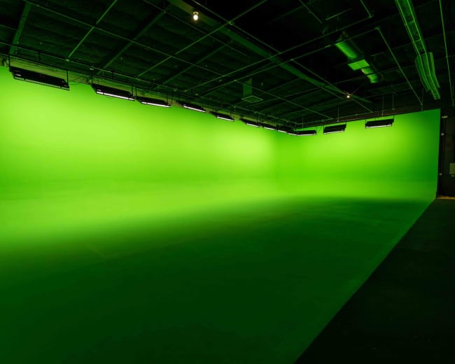 The image shows a large studio space with a bright green backdrop and overhead lighting.