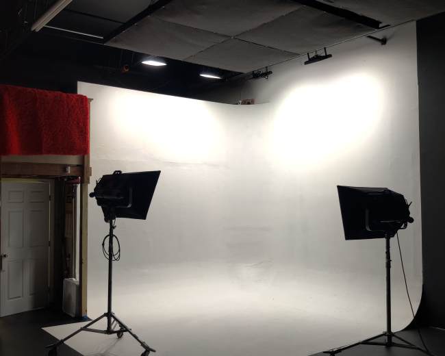 The image shows a photography studio with two lights on stands positioned in front of a white backdrop.