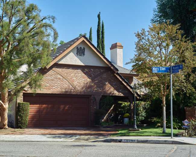 A residential home with a brick facade and a two-car garage sits at the corner of Mary Ellen and Keren Place, surrounded by trees and landscaping.