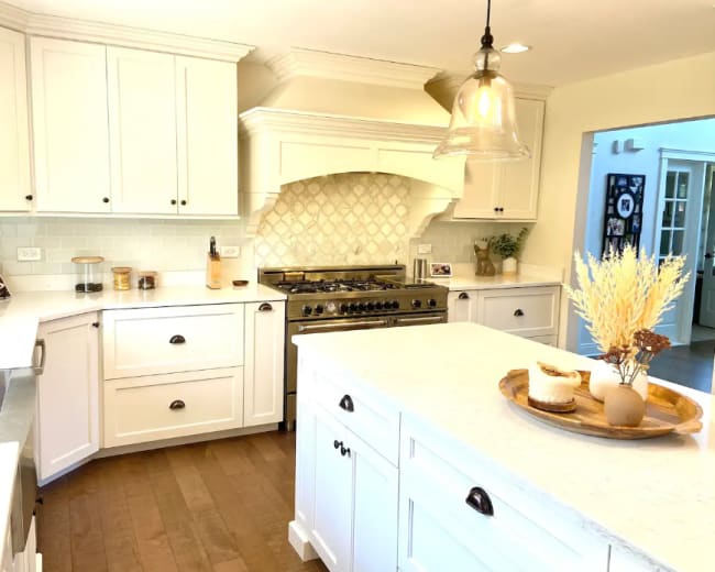 The kitchen features white cabinetry, a large island, and a stainless steel range with a decorative hood.