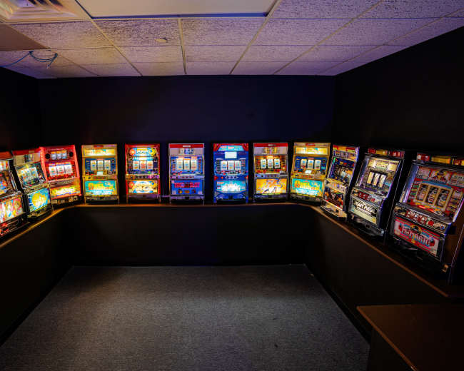The image shows a corner of a room filled with multiple brightly lit slot machines arranged along the walls.