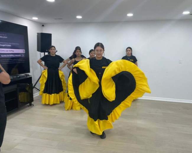 A group of dancers performs in a dance studio, wearing black and yellow traditional costumes.