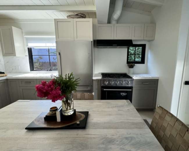 A modern kitchen features gray cabinetry, a stainless steel range, and a wooden dining table with a floral arrangement.