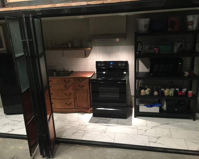 The image shows a modern kitchen with a black stove and oven, a stainless steel range hood, a wooden cabinet, and various kitchen appliances on black shelves.