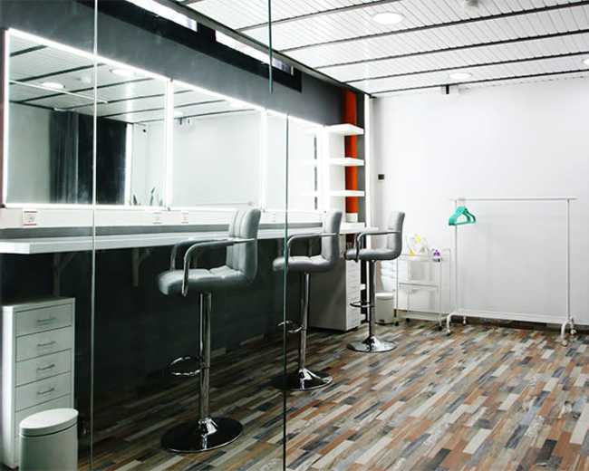 The image shows a modern dressing room with a mirrored wall, two barstools, and a clothing rack against a white background.