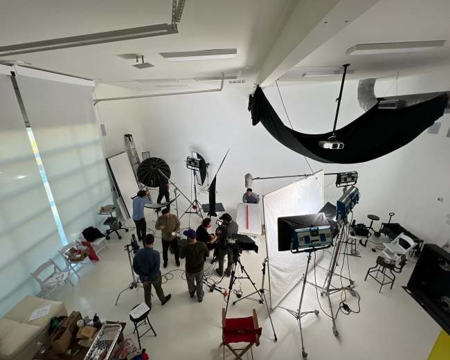 A film crew sets up equipment in a bright studio for a production shoot.