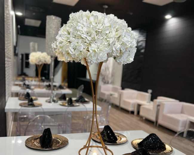 A dining setup features elegant tables adorned with gold and black decor, including floral centerpieces and plates with dark napkin arrangements.