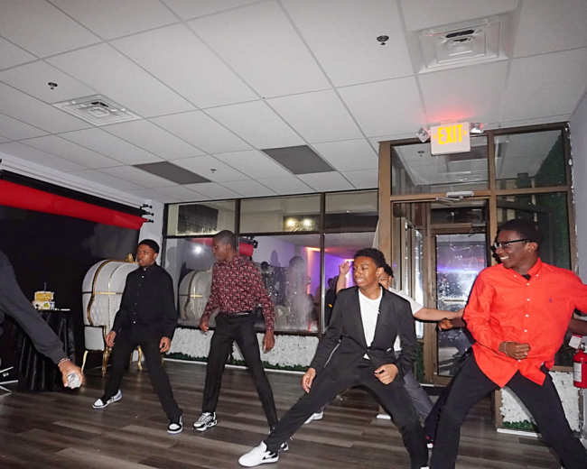 A group of young men dance in a dimly lit room with a festive atmosphere.