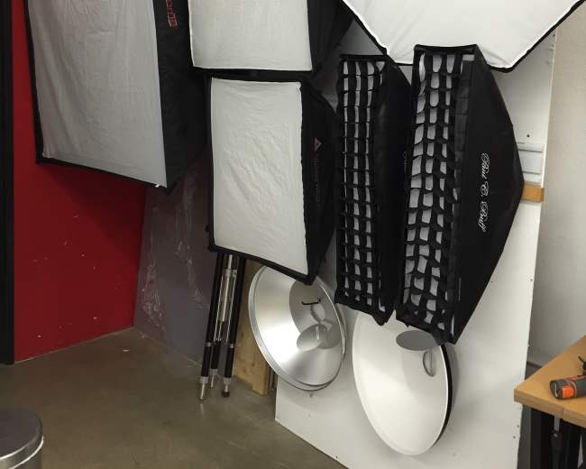 The image shows various photography light softboxes and equipment mounted against a red and white wall.