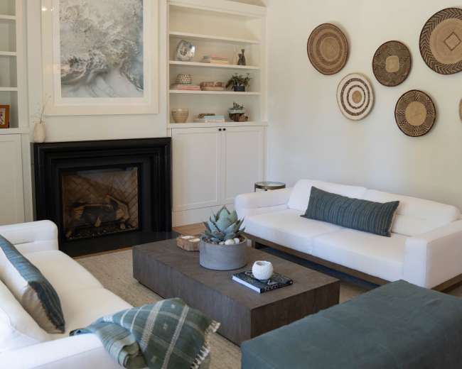 The living room features two white sofas, a wooden coffee table, a fireplace, and decorative wall hangings.