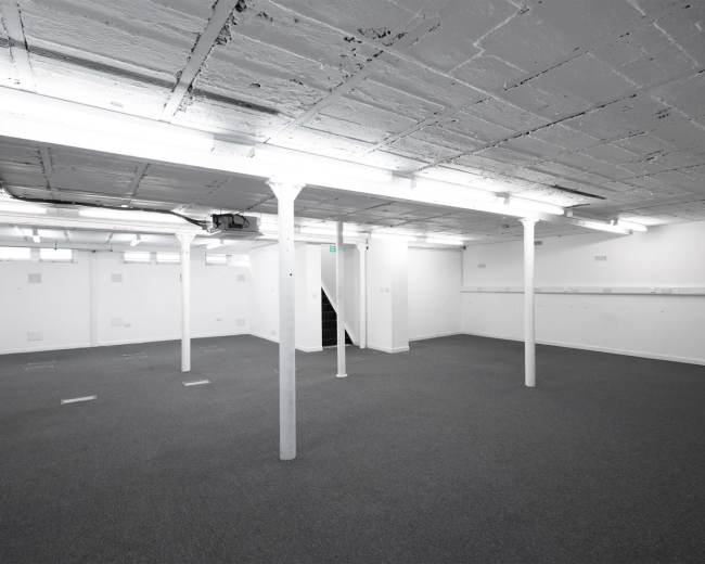 The image shows a spacious, empty basement with concrete pillars and bright overhead lighting.