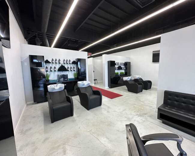 A modern salon interior featuring black styling chairs, wash stations, a red carpet, and a minimalist design with white walls and overhead lighting.