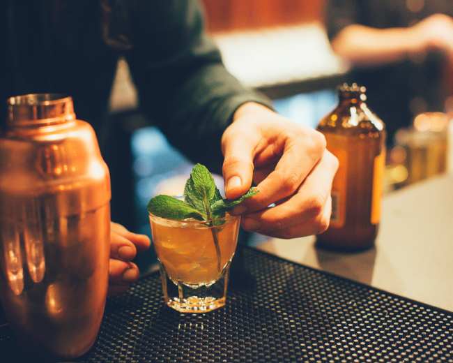 A bartender garnishes a cocktail with a sprig of mint in a dimly lit bar.