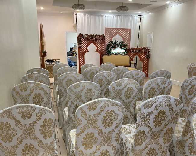 A row of elegantly covered chairs arranged in a well-lit event space, with a decorative backdrop at the front.