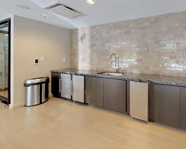 The image shows a modern kitchen with a dark cabinetry, a stainless steel sink, and a tiled backsplash.
