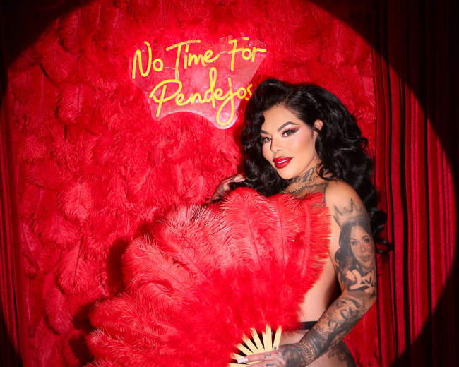 A woman poses with a large feather fan in front of a red textured wall featuring the words "No Time For Regrets."
