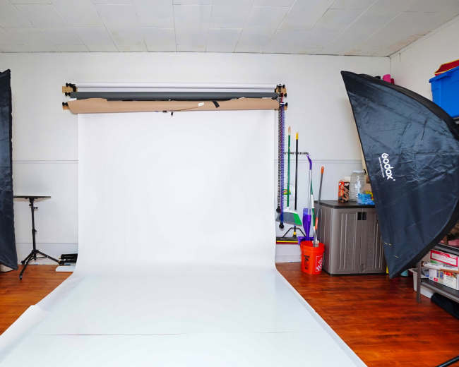 The image shows a photography studio setup with two large softbox lights flanking a white backdrop and a smooth floor.