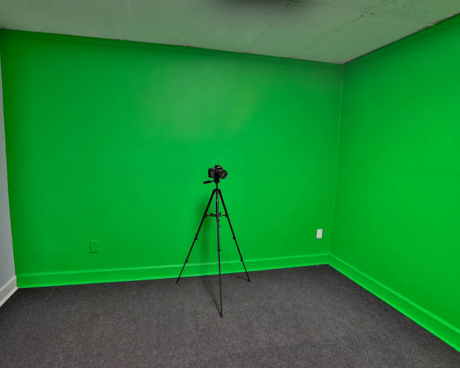 A room with a bright green wall, featuring a camera mounted on a tripod in the center.