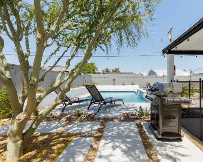 A backyard features a swimming pool, lounge chairs, and a grill, surrounded by trees and landscaping.