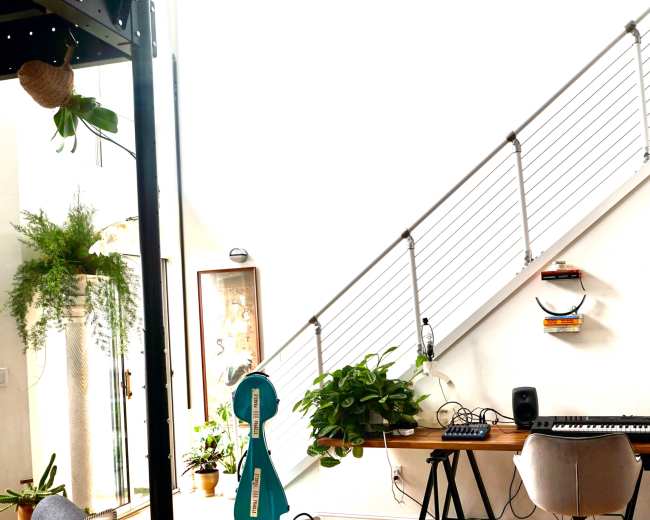 A modern interior features a staircase, a small desk with musical equipment, and decorative plants.