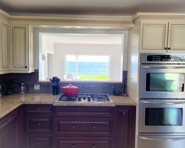 A kitchen with dark wood cabinets and granite countertops has a view of the ocean through a large window.