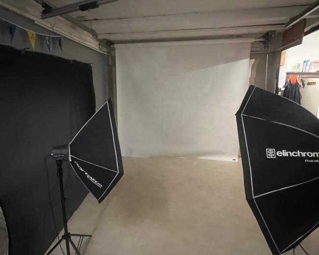 A photography studio setup features two light umbrellas positioned on either side of a blank white backdrop.
